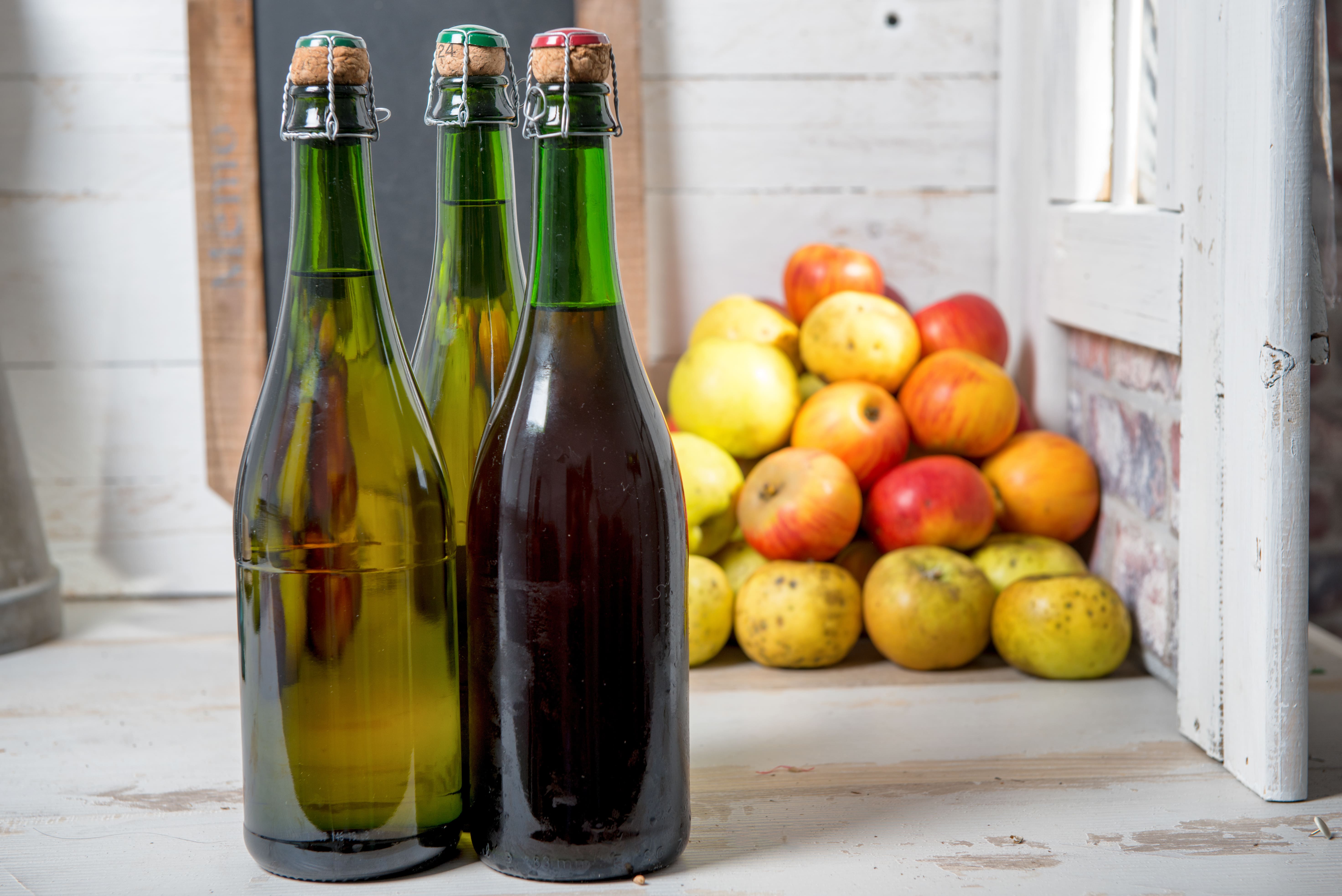 Three bottles of cider with apples stacked in the background