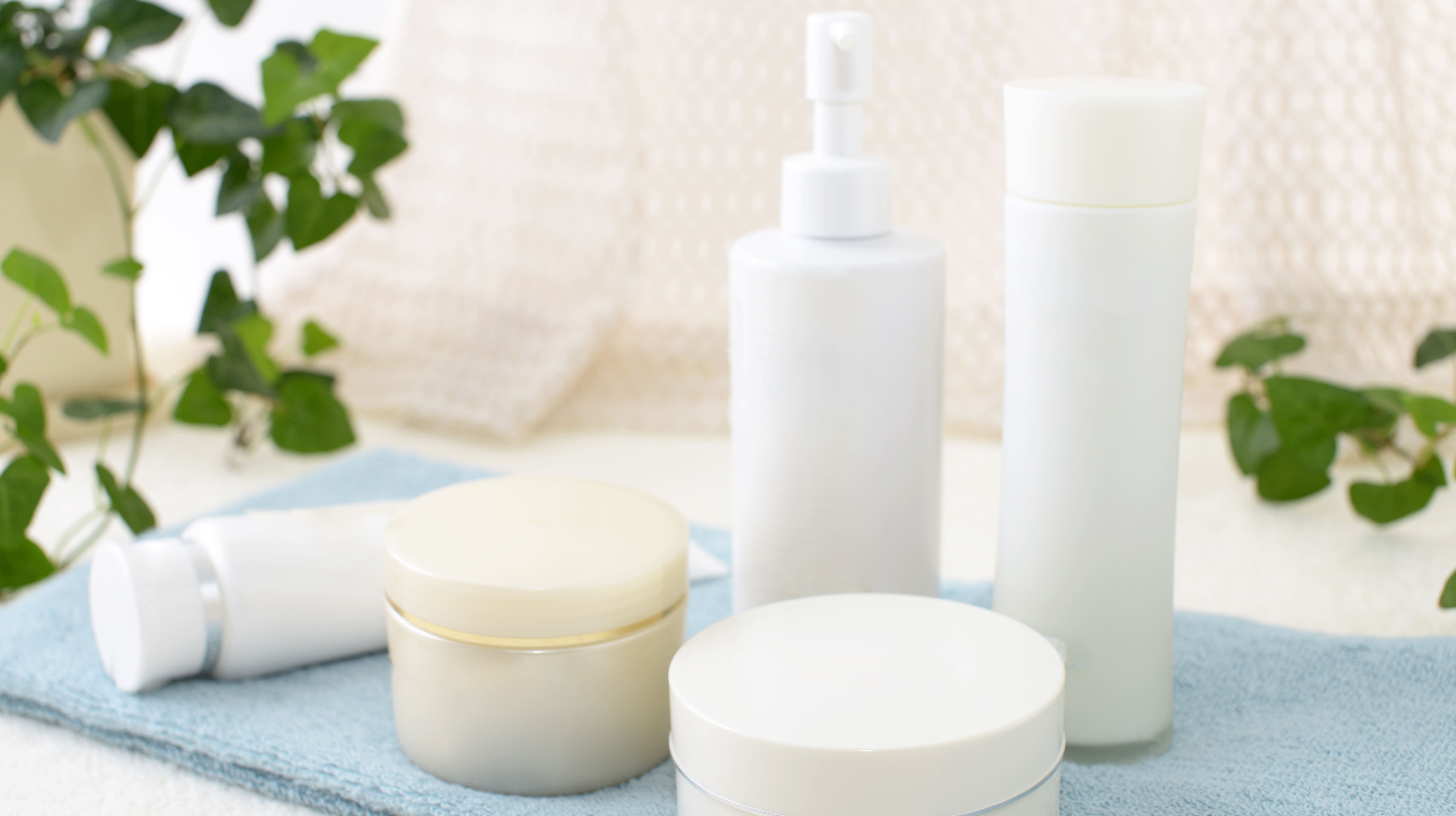 Various cosmetic products in creme packaging on a blue cloth, with green leaves in the background.
